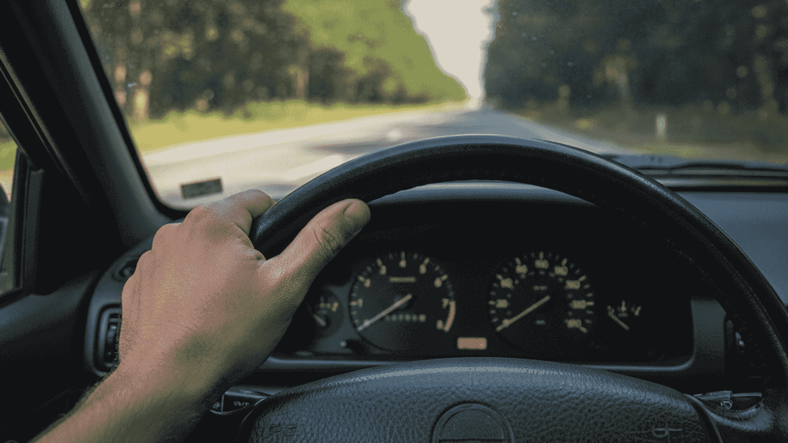 Ruka vozača na volanu evropskog automobila sa instrumentnom tablom koja prikazuje niske obrtaje tokom mirne vožnje po dvotračnom putu